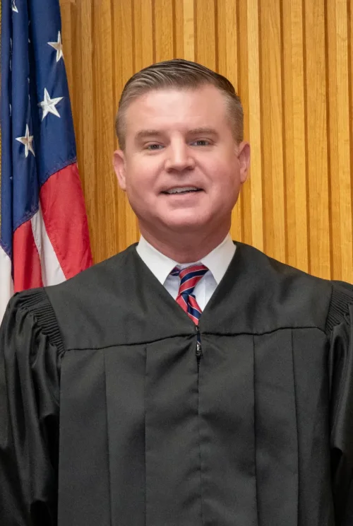 Judge Warren McSweeney in judicial robes before the United States flag